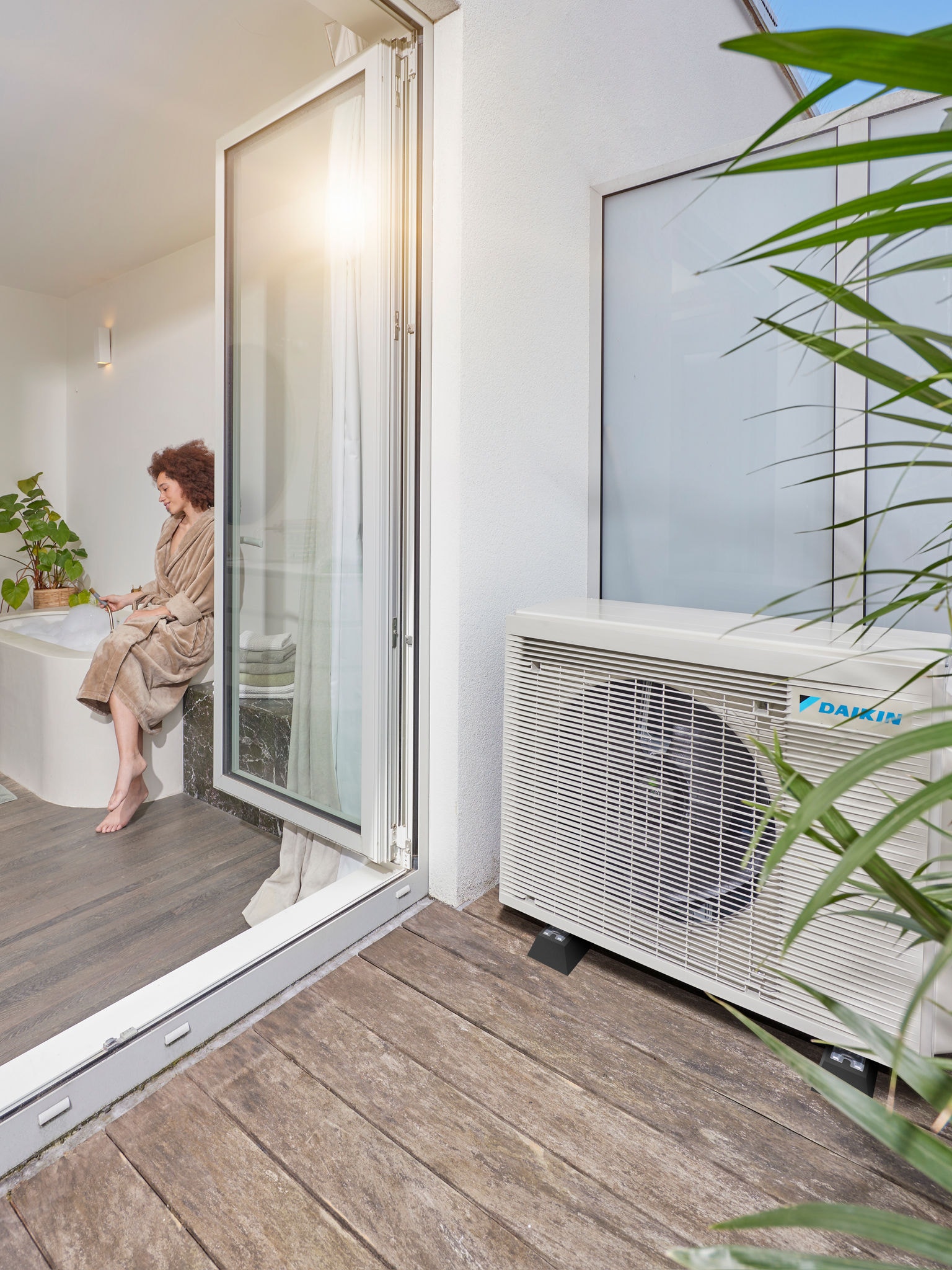 Luchtwarmtepomp geïnstalleerd naast een terras met geopende deuren naar een moderne badkamer
