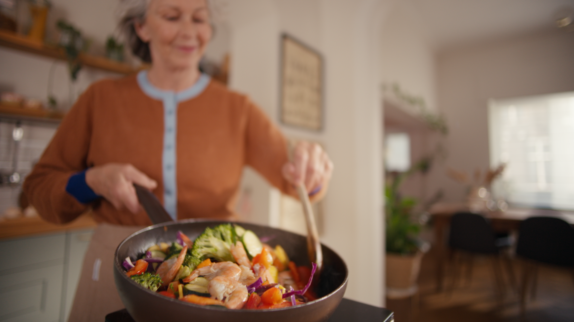 Een lachende vrouw die een wokgerecht met garnalen maakt waarbij kookgeurtjes ontstaan