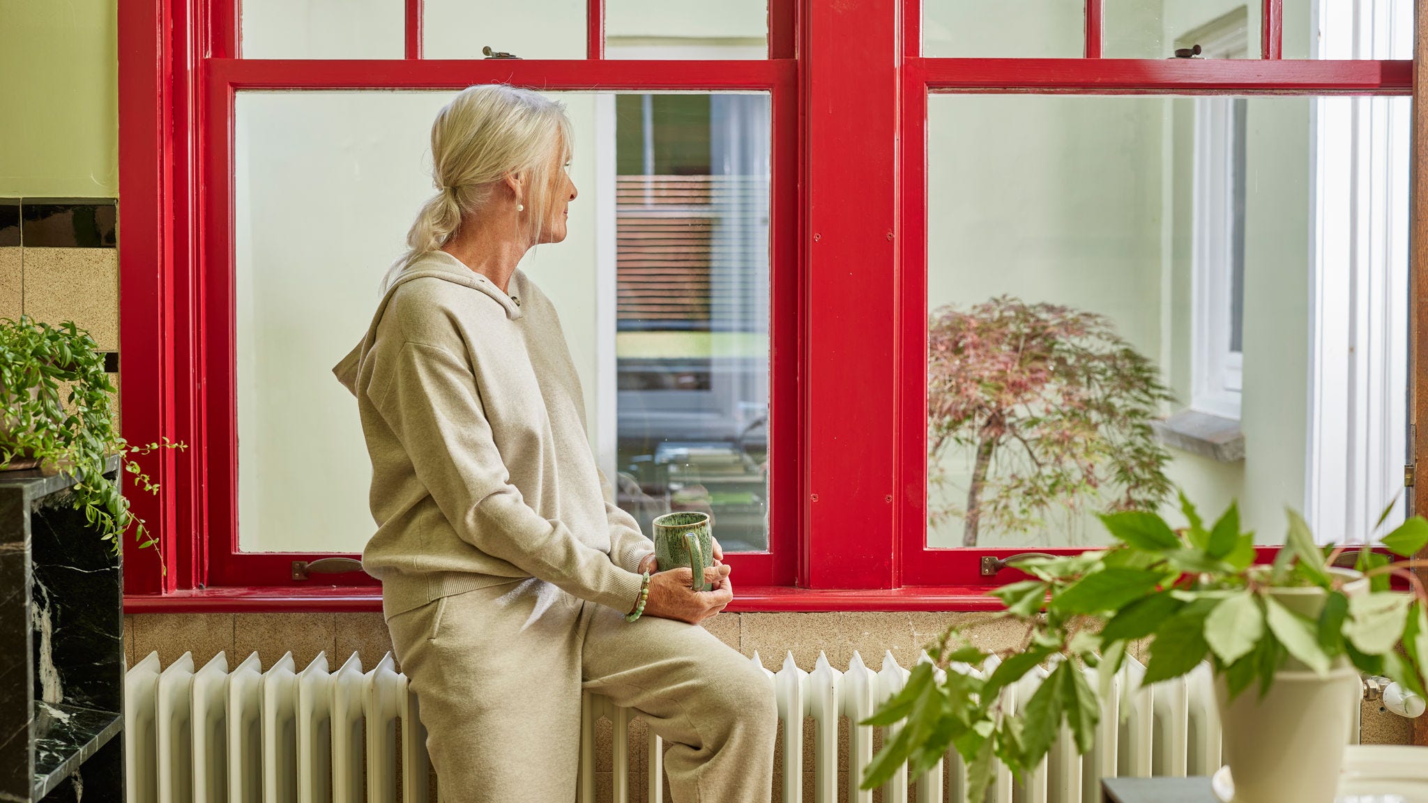 Vrouw die op een radiator zit bij een groot raam en van een warme, energiezuinige woning geniet