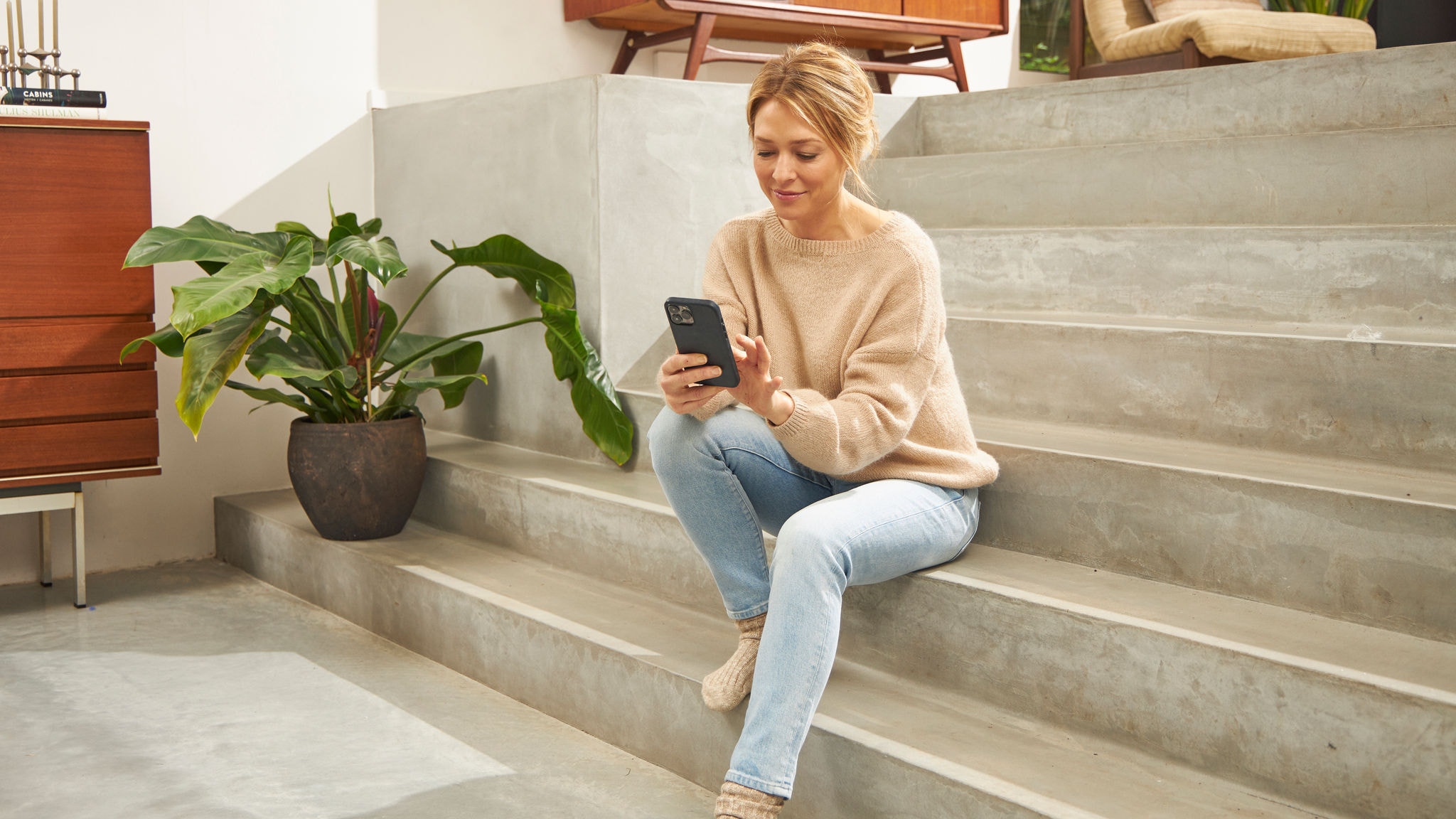 Een vrouw zittend op de trap in haar huis, terwijl ze de Onecta app gebruikt op haar mobiele telefoon