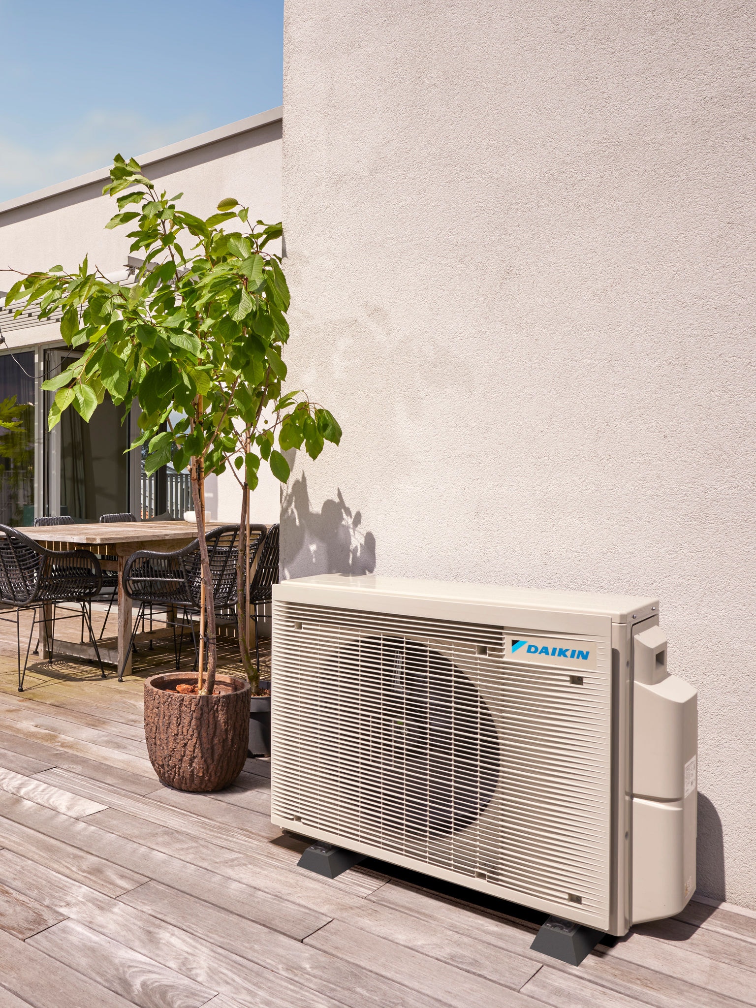 Warmtepomp buiten discreet tegen een muur geplaatst, in de schaduw van bomen