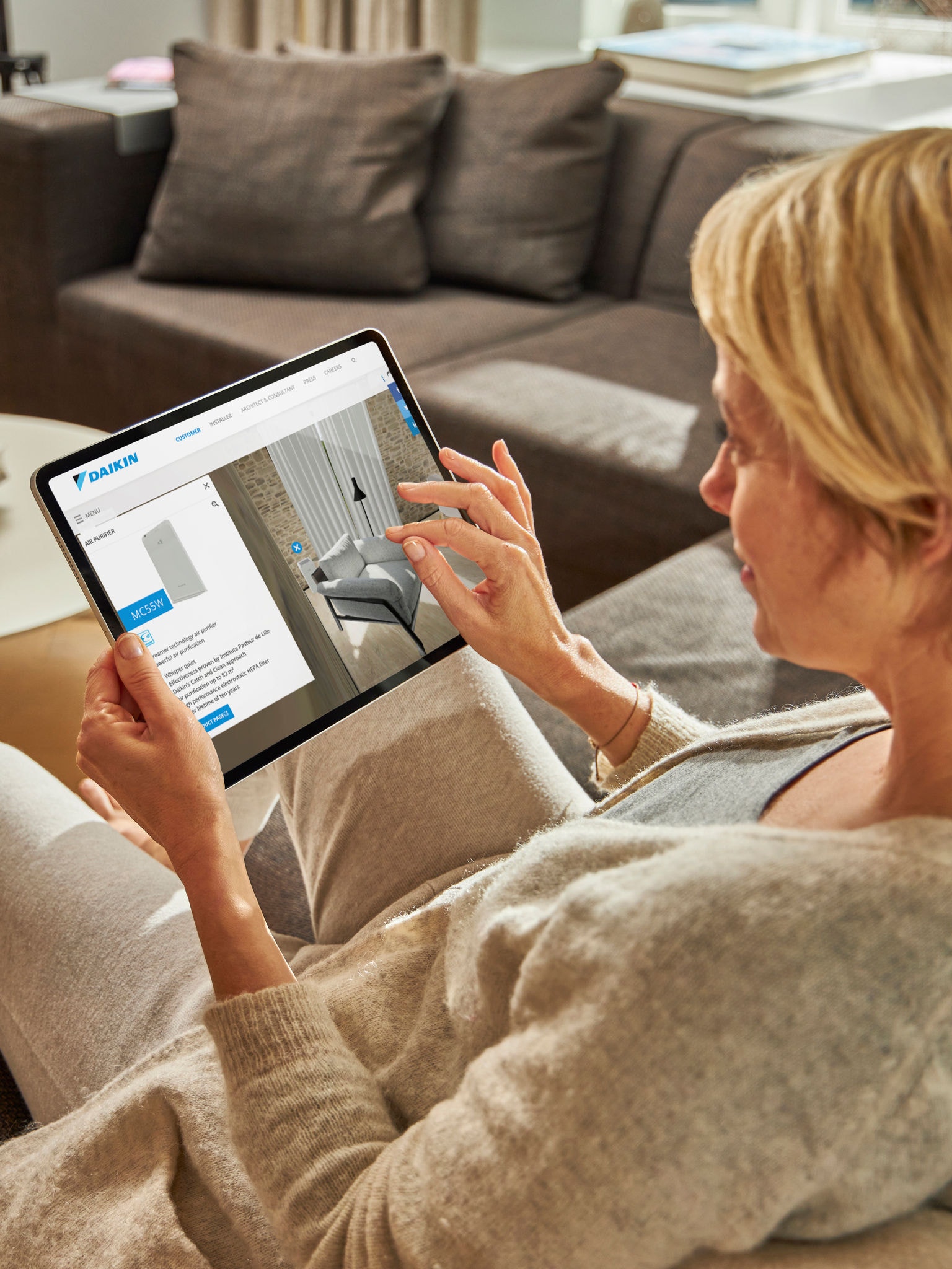 Een vrouw zit op een bank en bekijkt airconditioners in de virtuele showroom op haar tablet