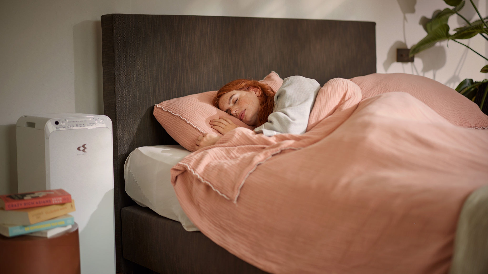 Een vrouw slaapt vredig in een knus bed, terwijl vlakbij een luchtreiniger zorgt voor schone luchtkwaliteit in een slaapkamer in de winter
