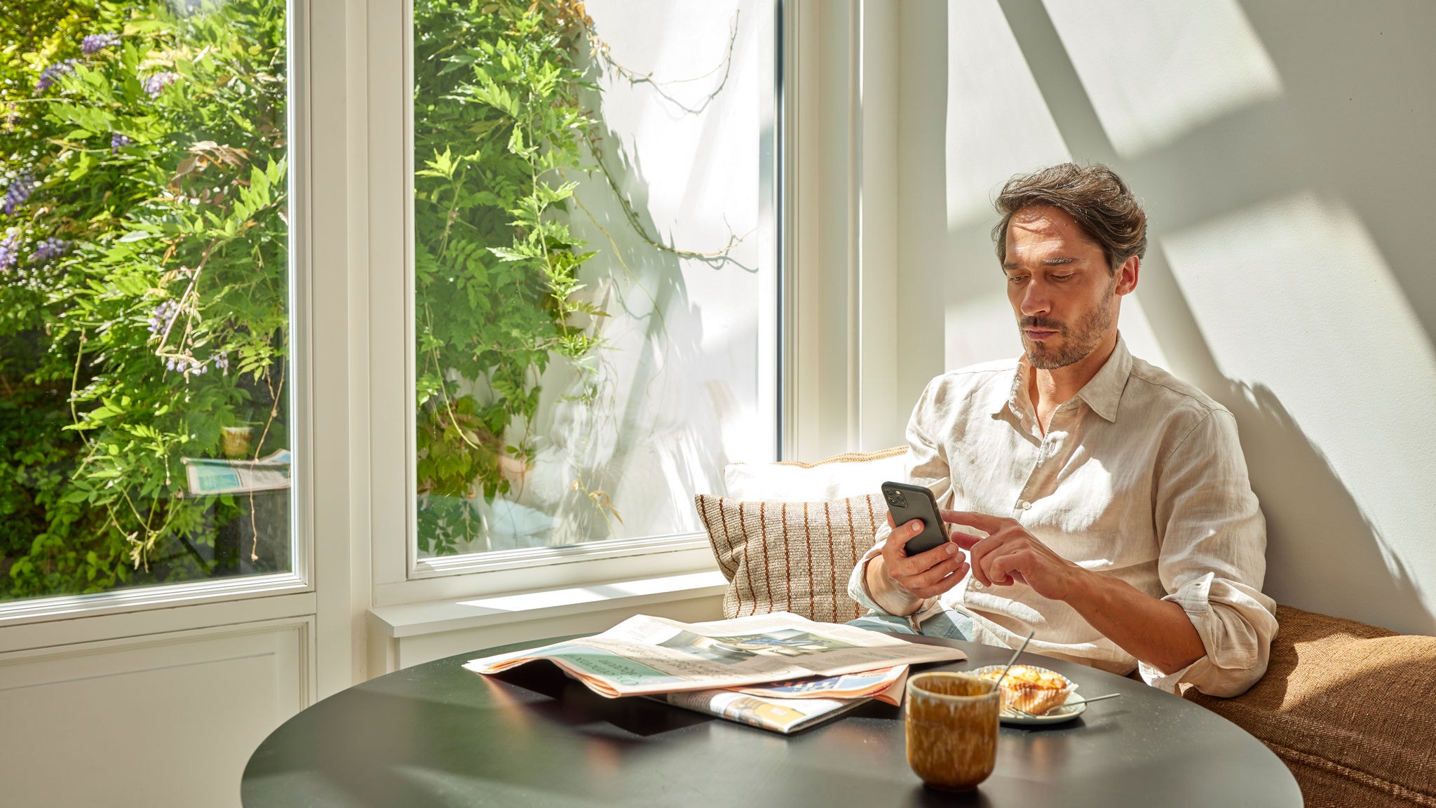 Een man in een licht huis die zijn smartphone gebruikt om de airconditioner te bedienen, voor energiezuinig comfort