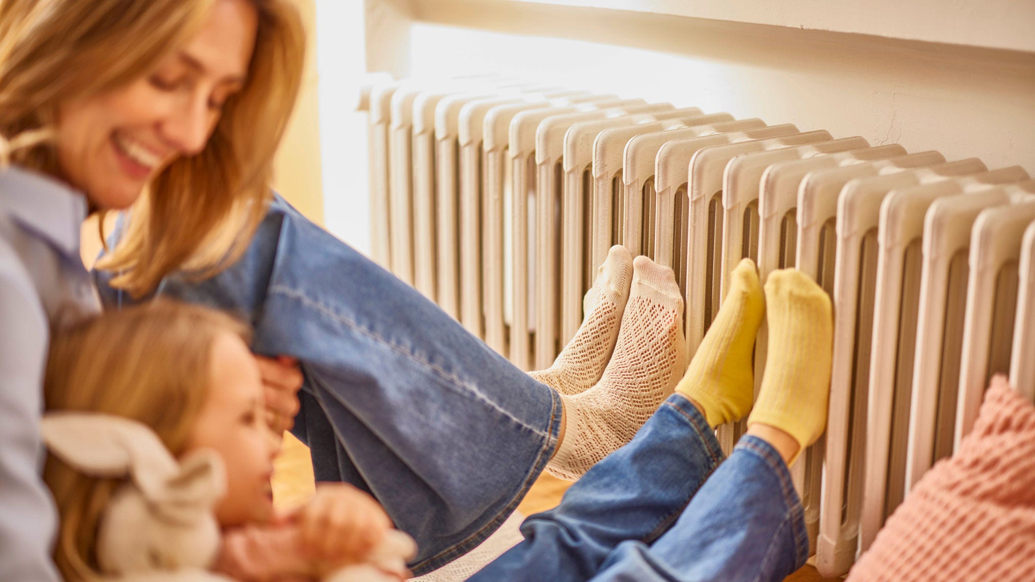 Moeder en dochter warmen hun voeten aan een radiator in een warme en comfortabele woning