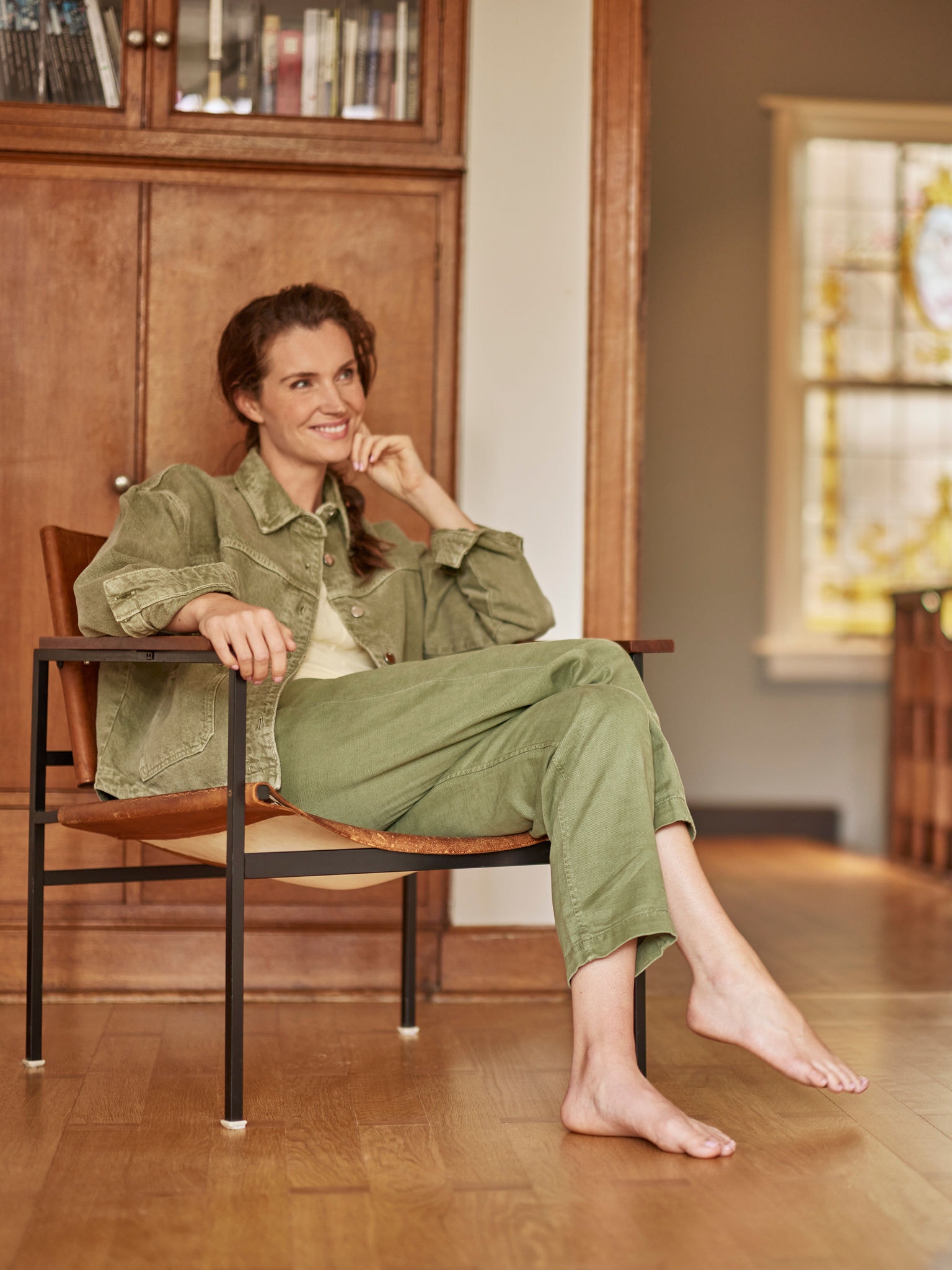 Vrouw zit met blote voeten in haar fauteuil en kijkt glimlachend voor zich uit.