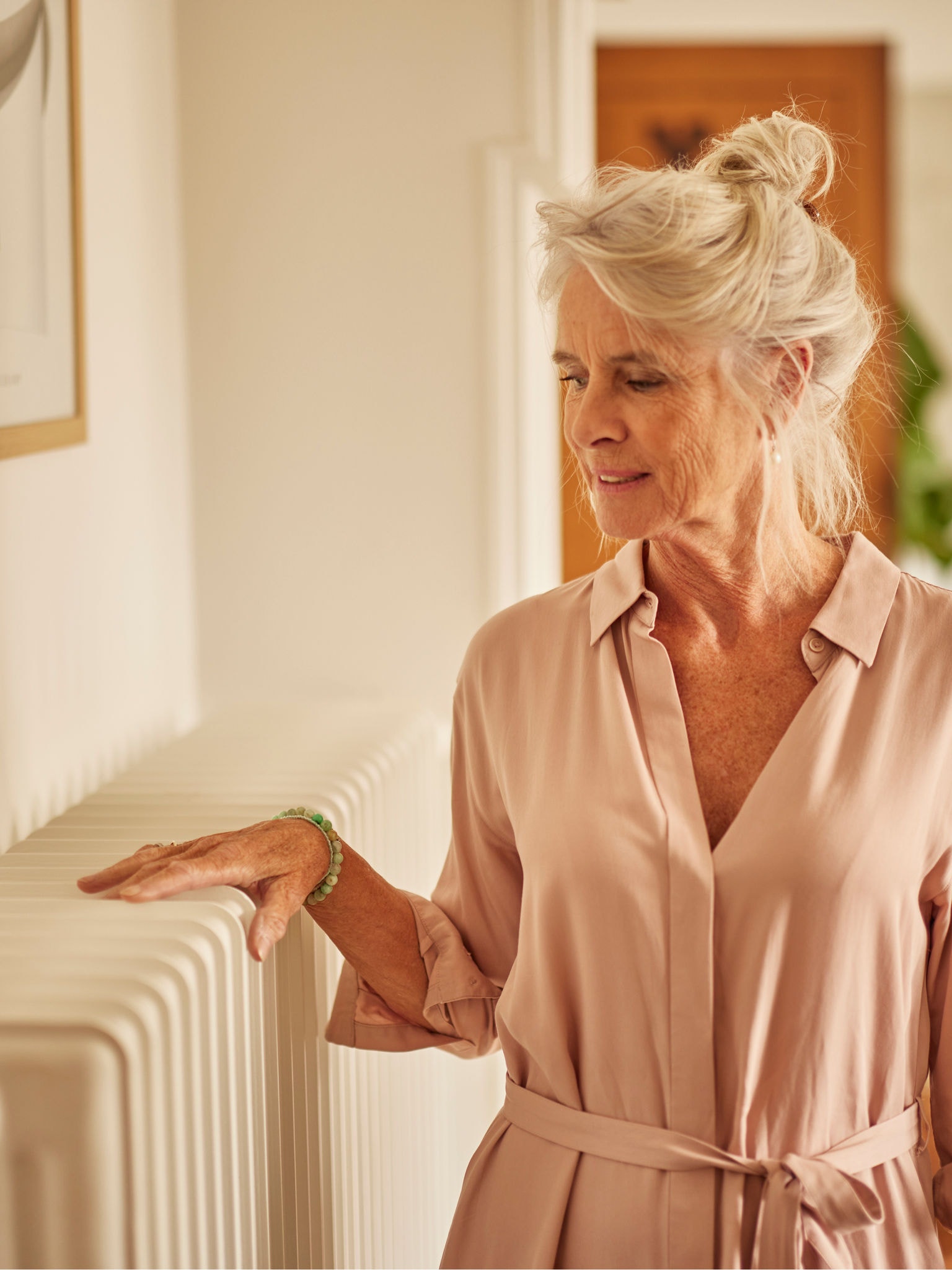 Een vrouw warmt haar handen aan een radiator in de slaapkamer die samenwerkt met luchtwarmtepomp