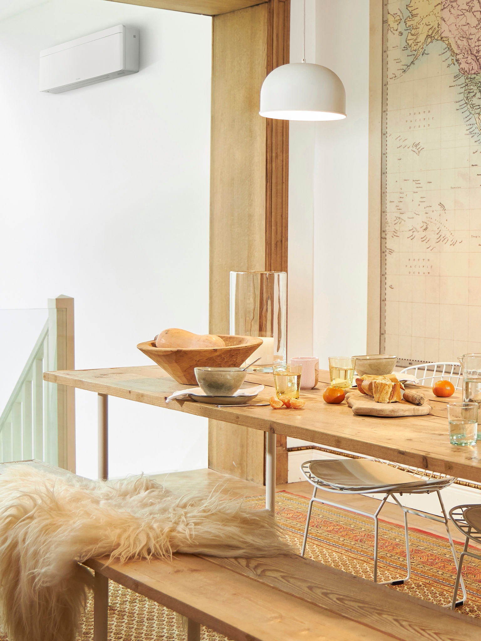 Tafel gedekt voor lunch met eten en fruit in een lichte ruimte, airconditioner zichtbaar bij de trap.