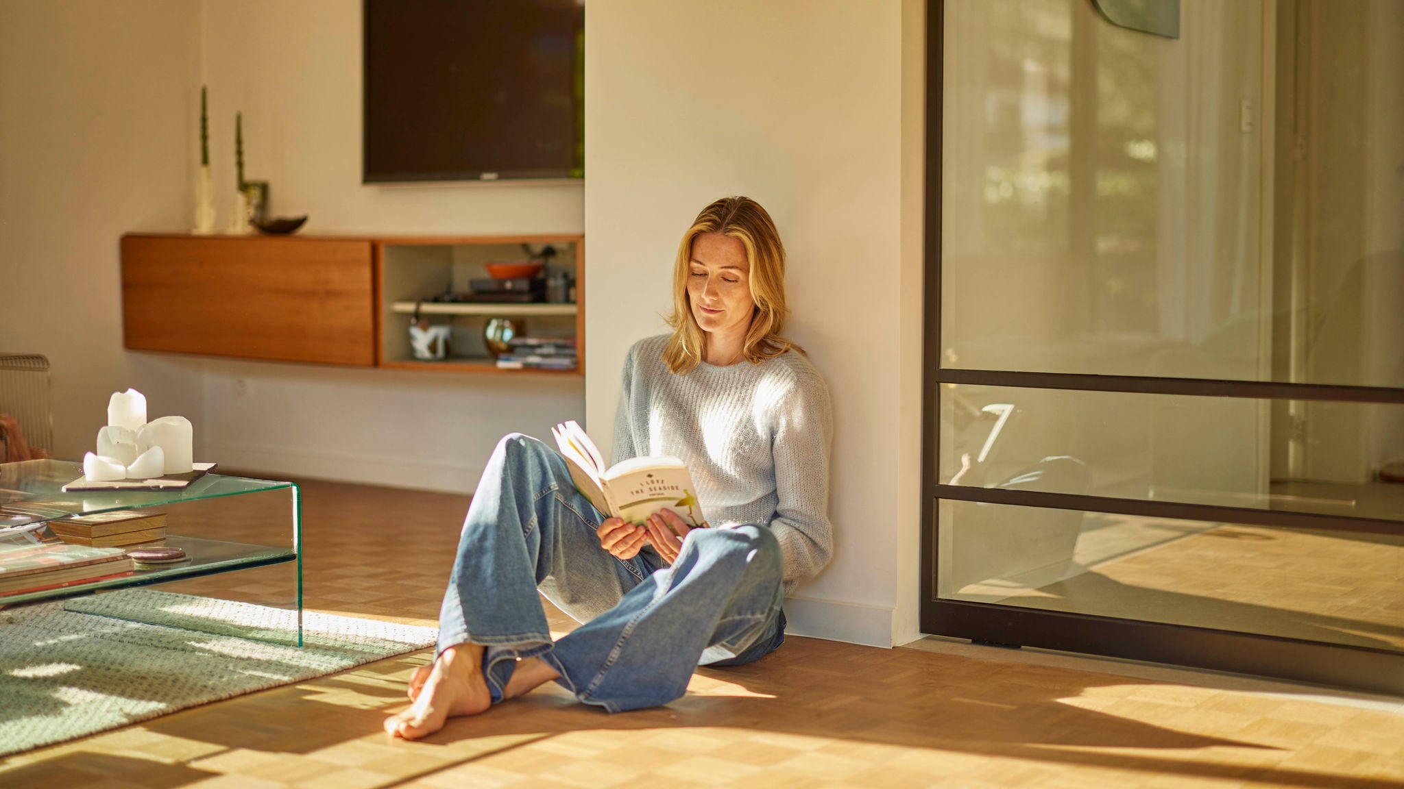 Een vrouw zit te lezen op een houten vloer met vloerverwarming en geniet van de perfect verwarmde kamer