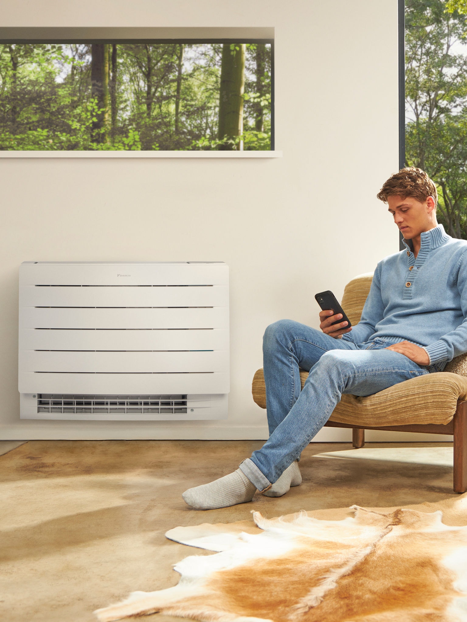 Een man in een lichte kamer die op zijn telefoon kijkt met aan de wand achter hem een warmtepomp