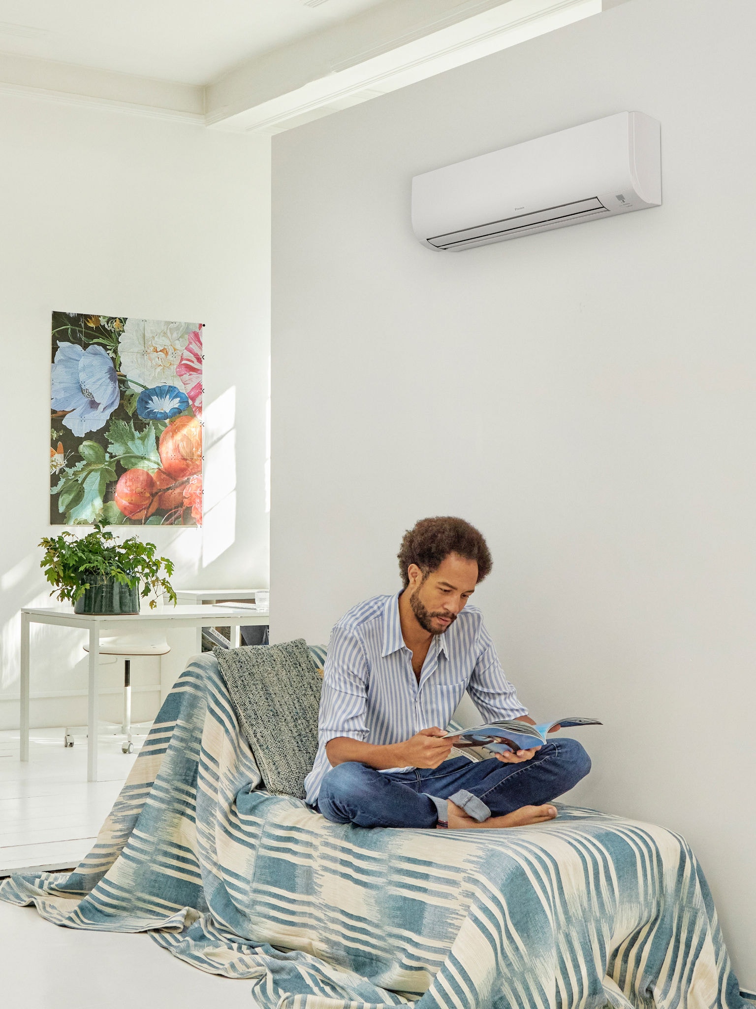 Een man leest in een heldere, moderne woonkamer met een warmtepomp aan de muur, om het comfort en energierendement te demonstreren van warmtepomptechnologie die wordt gesteund door stimuleringsregelingen van de overheid
