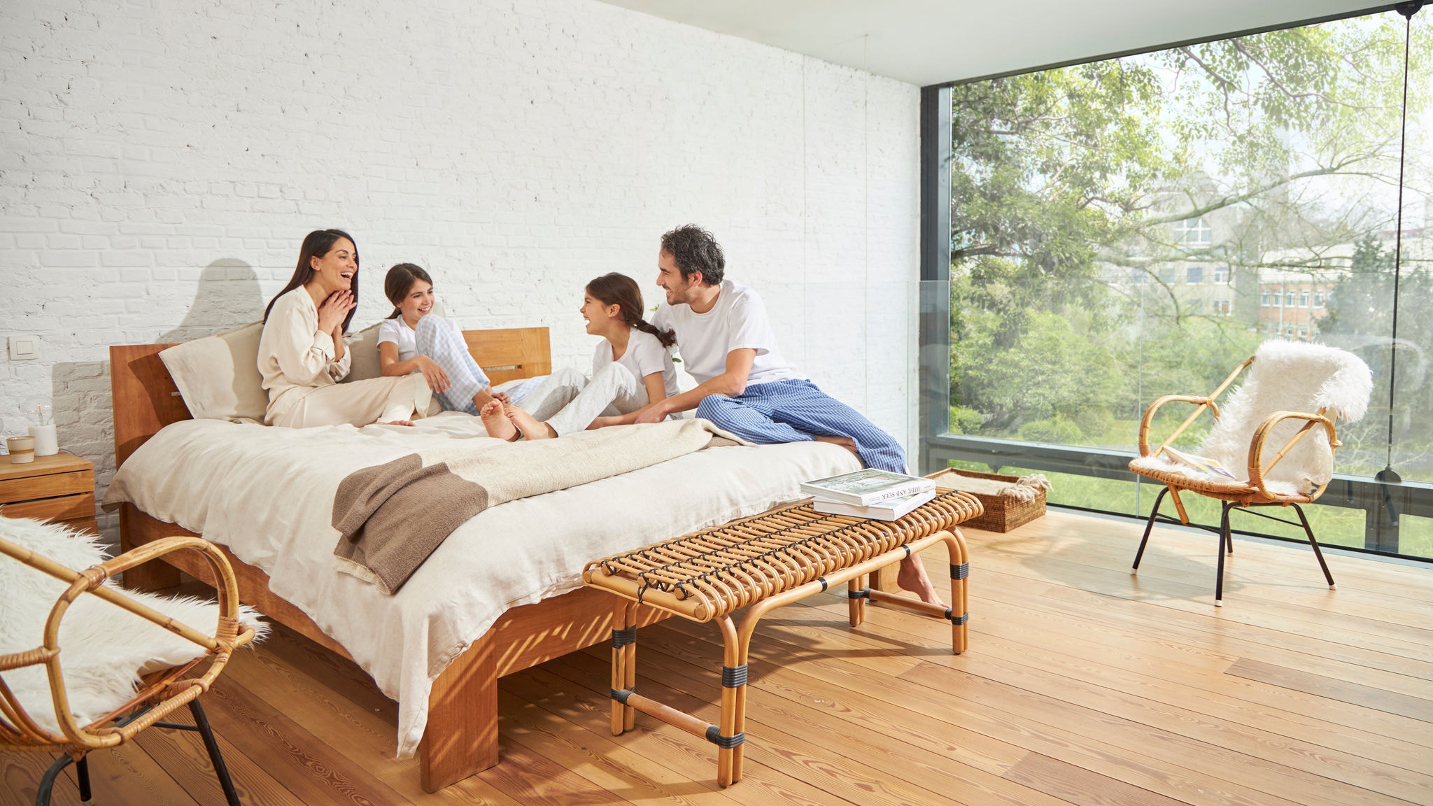 Gezinsleden in gesprek op bed in een slaapkamer met een grote glaswand, binnenluchtkwaliteit en veel daglicht
