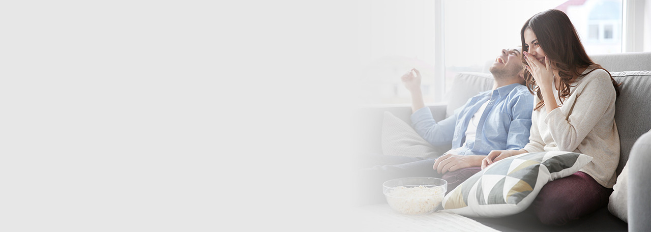 Lachend echtpaar met popcorn op een bank.